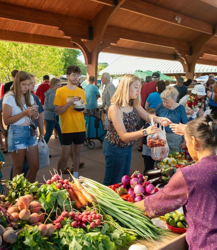 Woman purchasing a bag of strawberries from a stand selling multiple fruits and vegetables